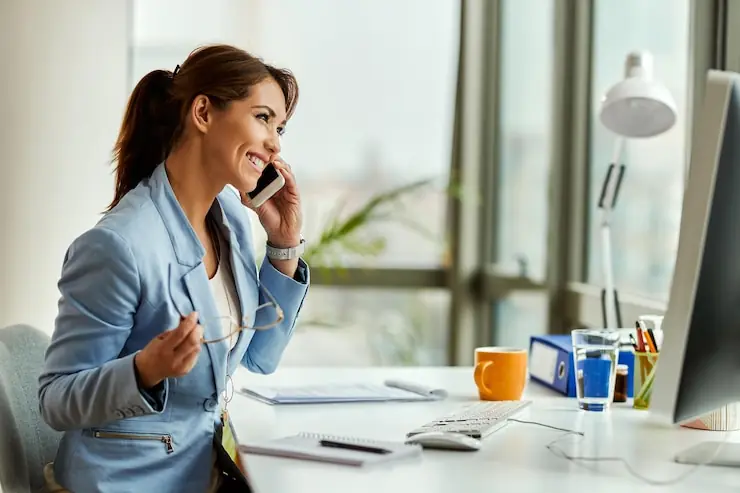 A woman smiling on a phone call at her office desk