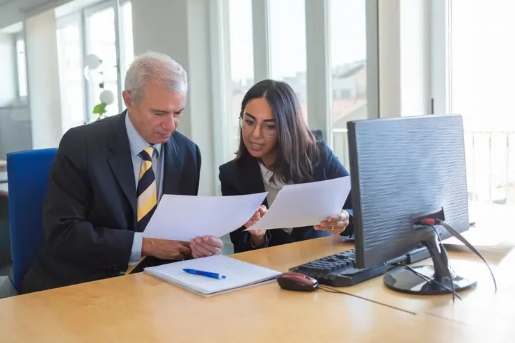 Two colleagues at a desk discussing a client agreement